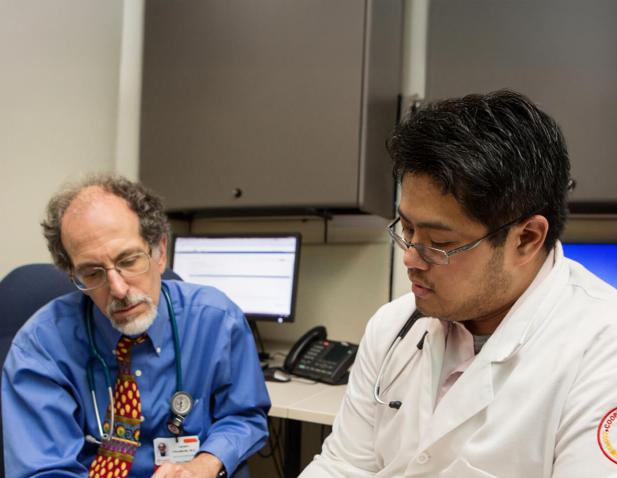 Two physicians reviewing information together in a medical office, with computers and phones in the background.
