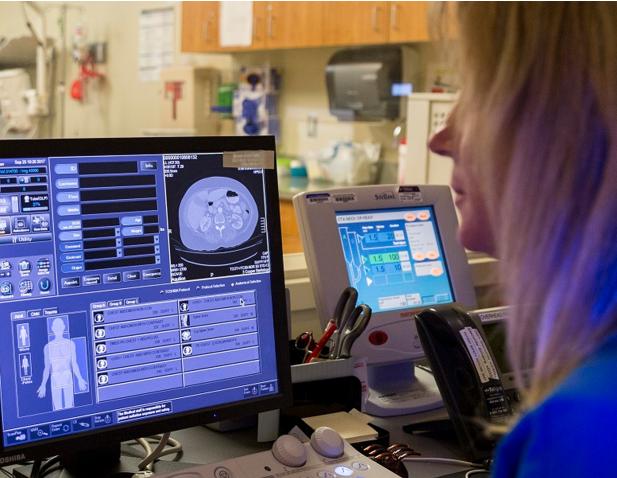 Medical professional reviewing a CT scan on a computer monitor, with diagnostic imaging software and patient data displayed in a hospital setting.