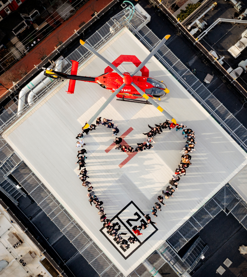 A bird's eye view of the Cooper helipad with team members standing to form the shape of a heart, and the Air Cooper helicopter grounded above them.