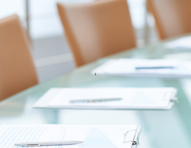 Empty chairs pushed into a table with notes and pens at each seat in preparation for a meeting.