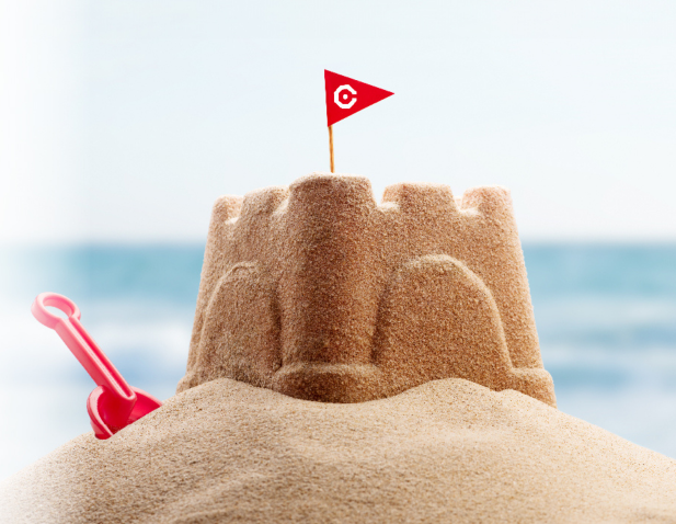 A sandcastle with the ocean in the distance, a red shovel to the side, and a red pennant flag with the Cooper "C" icon in white. 